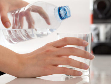 Female hands pouring bottled water into glass